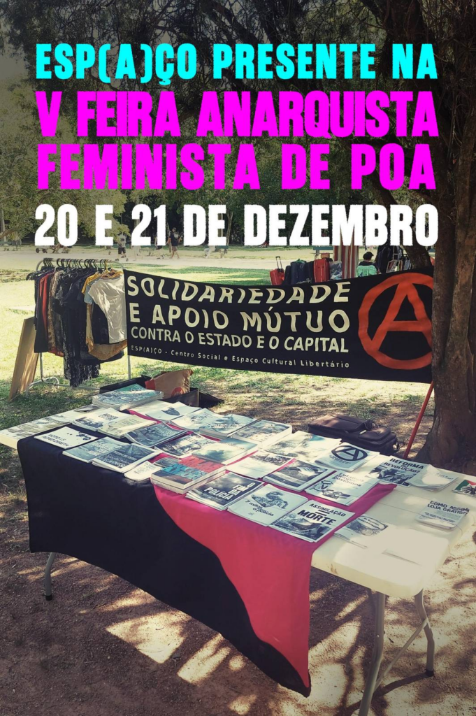 Foto de uma mesa sobre um gramado. Sobre a mesa uma bandeira negra e rosa. E sobre ela diversos zines, livros e panfletos, sobre a foto o texto Esp(a)ço Presente na V Feira Anarquista Feminista de Porto Alegre
