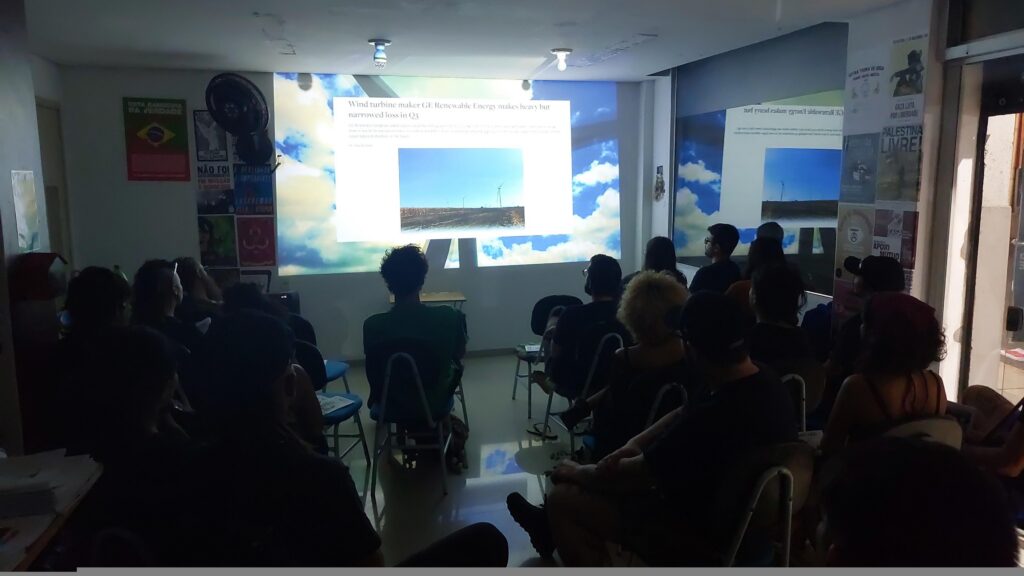 Várias pessoas no escuro de sentadas de costas para a câmera, assistindo à projeção de um filme.